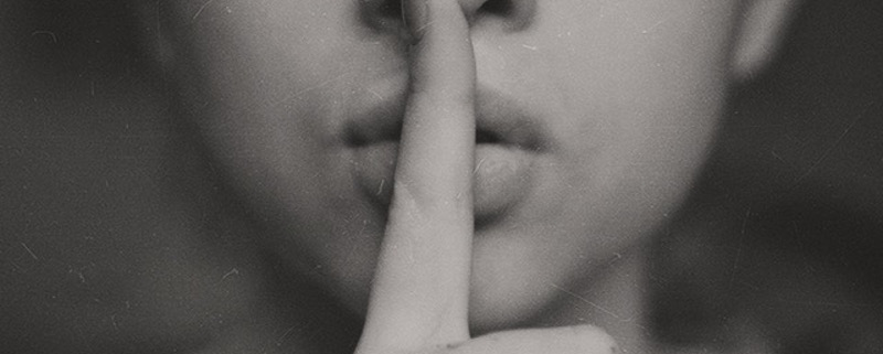 Schweigen ist nicht immer Gold - Weiblicher Mund mit dem Finger auf den Lippen