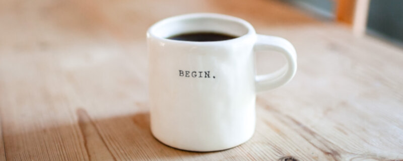Kaffeetasse auf einem Holztisch, beschriftet mit dem englischen Wort Begin
