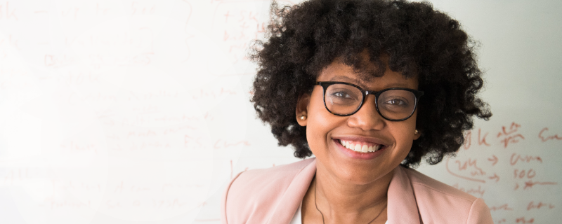 Junge Frau mit schwarzen Locken vor einem Whiteboard