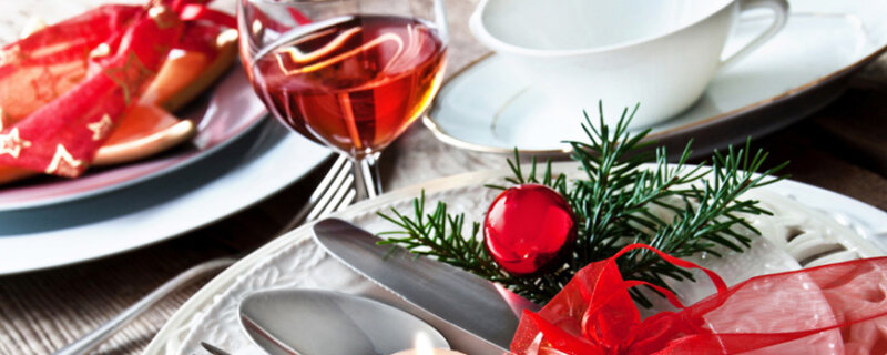 Weihnachtsgedeck mit Weinglas, Teetasse, Teller, Besteck und Tannenzweig