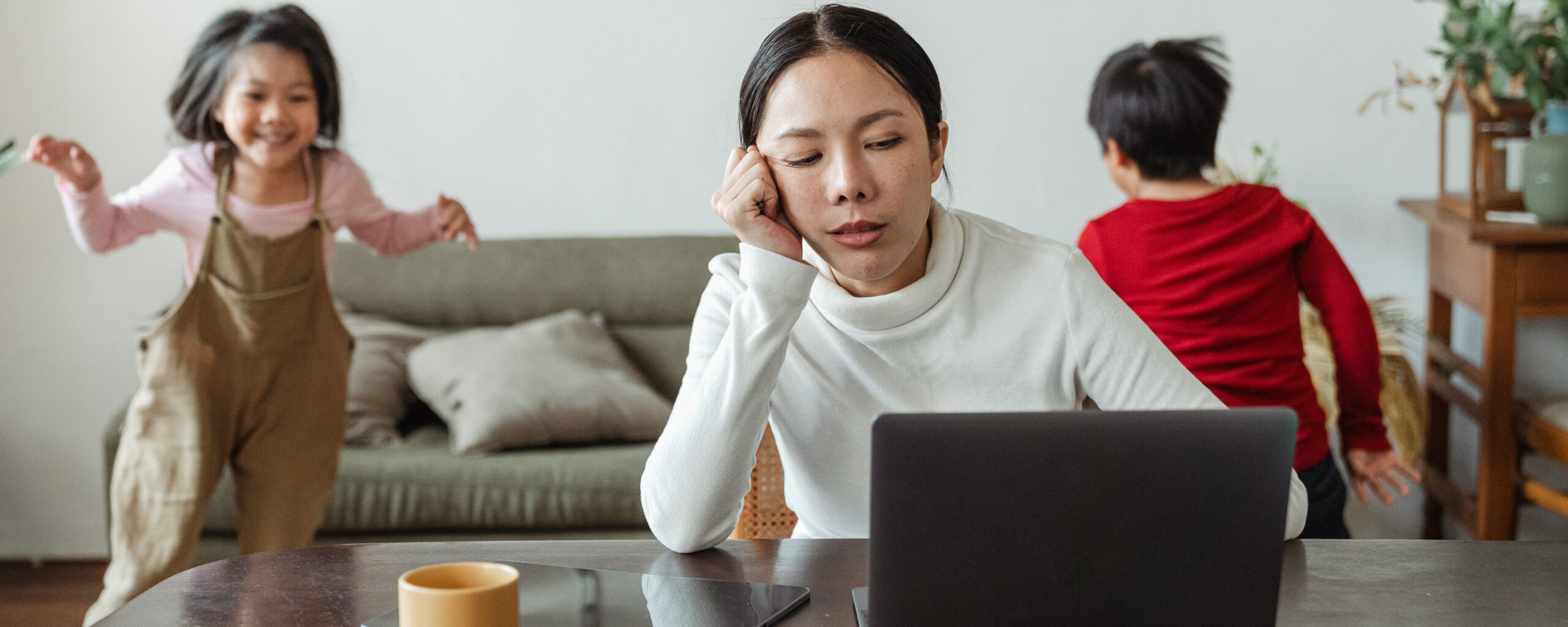 Frau im Homeoffice mit zwei spielenden Kindern im Hintergrund